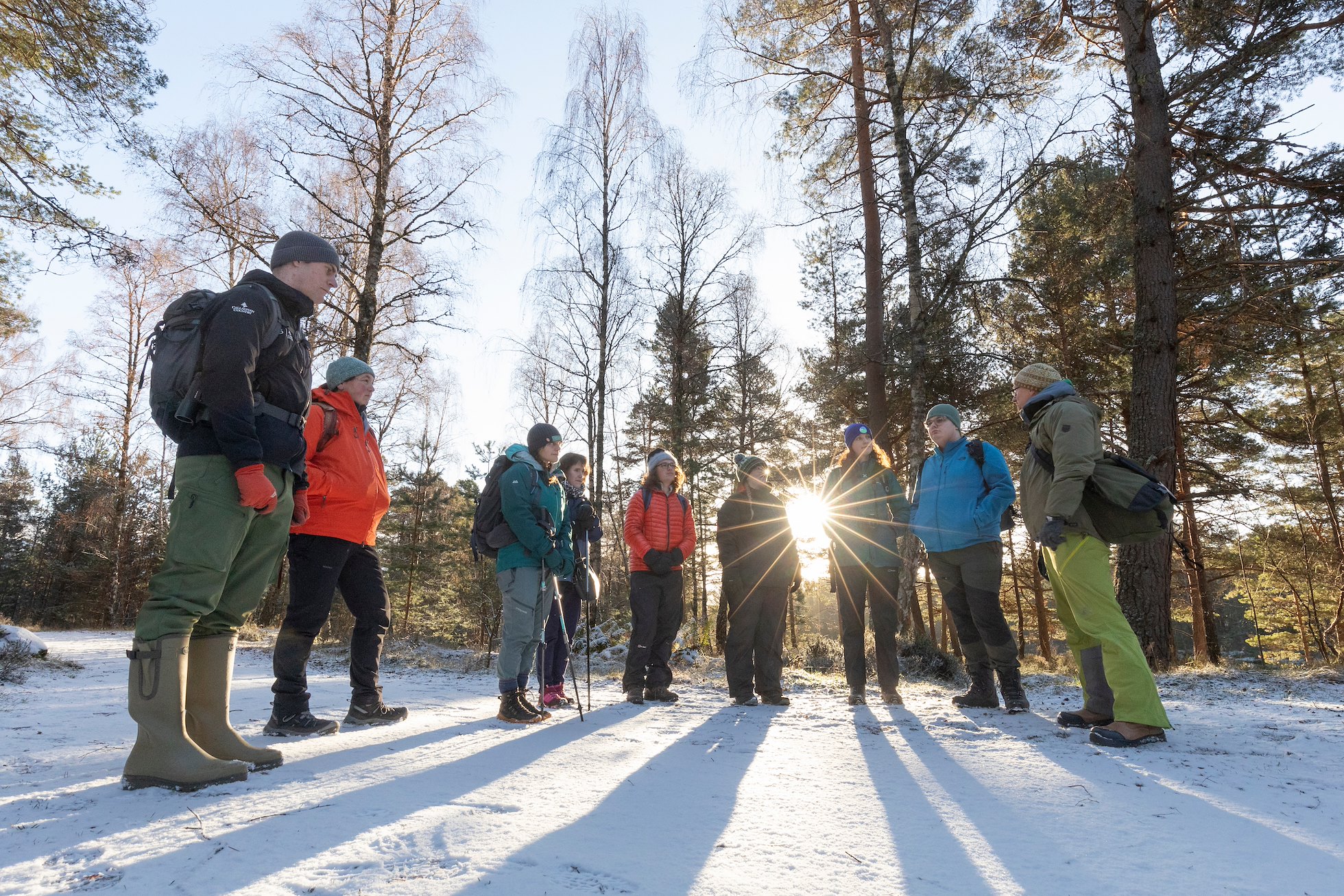 Group of people dressed in winter clothing in pine woodland setting, during an outdoor training session as part of a residential communications training course, November 2024